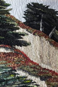 A close-up of a textile artwork depicting a landscape with textured trees, a sandy path, and greenery made from layers of fabric and thread in green, black, cream, and red tones.