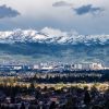 A panoramic view of San Jose's buildings surrounded by trees, with green rolling hills and snow-capped mountains in the background under a cloudy sky. Photo by Vlad Karpinsky