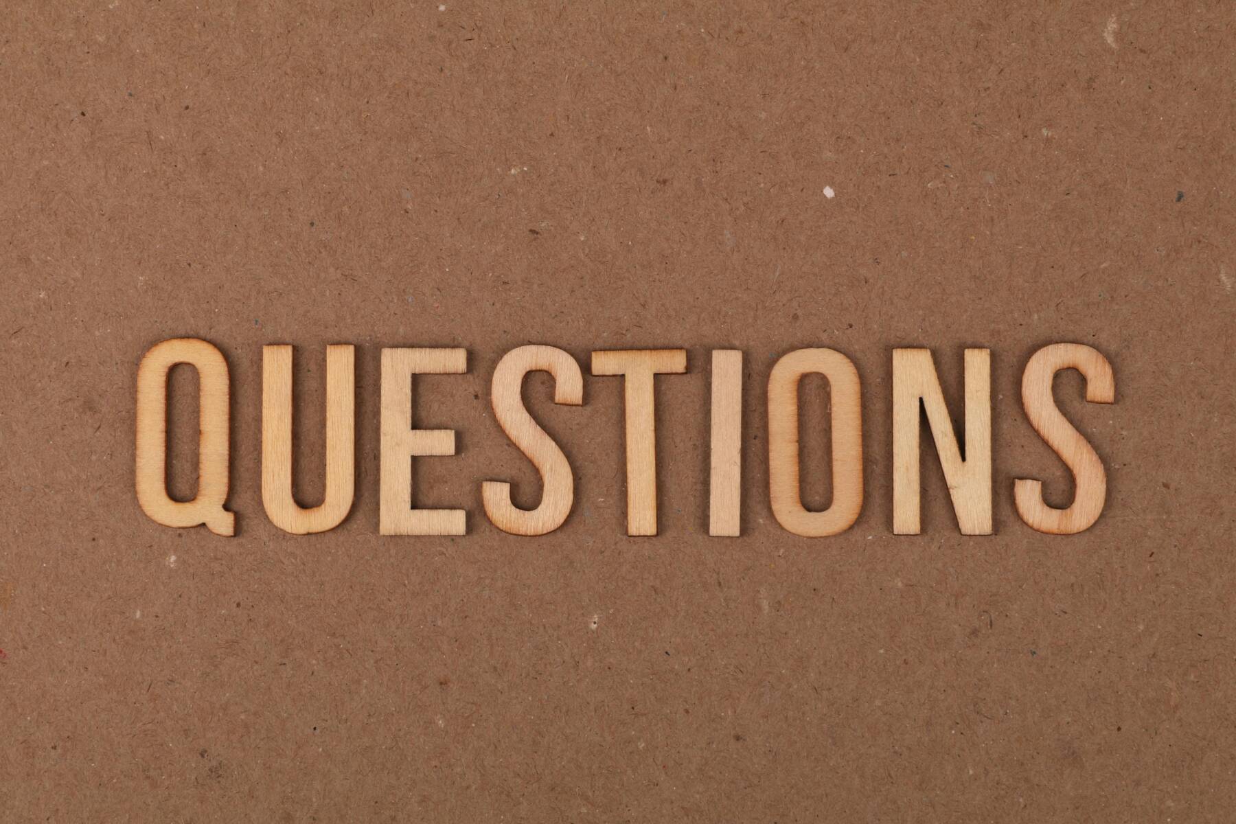 Wooden letters spelling QUESTIONS are arranged in a straight line on a brown, textured background.