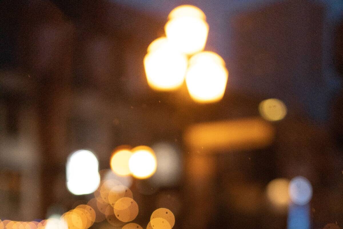 Out-of-focus streetlights and city lights create a warm, blurry bokeh effect at night, with a soft reflection of the glowing lights visible on a dark, shiny surface in the foreground.