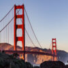 The Golden Gate Bridge in San Francisco is shown at sunset, surrounded by greenery, with hills and a clear sky in the background.