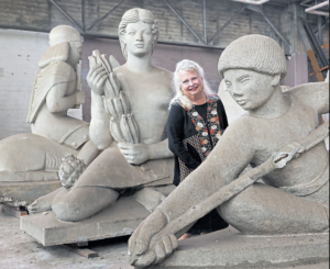 A woman stands in a studio among several large, unfinished concrete sculptures.